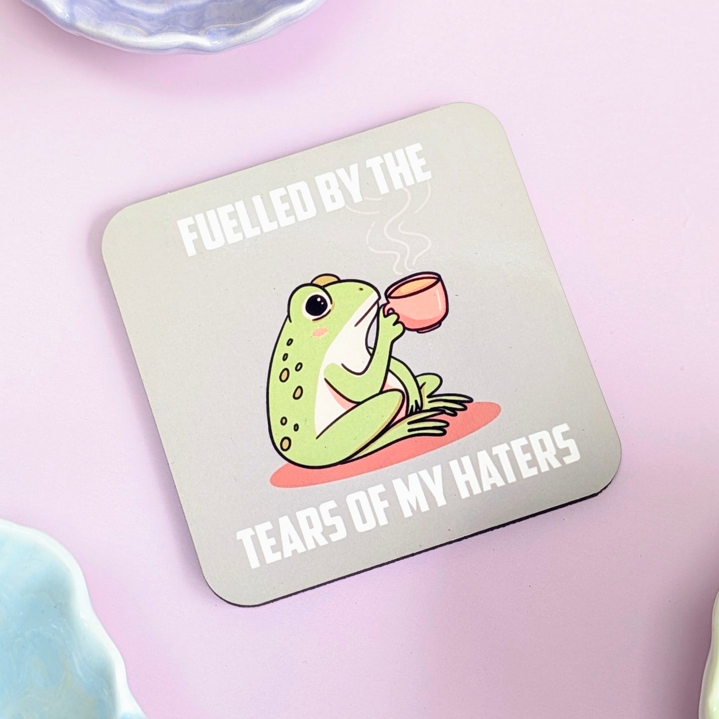Coaster with a frog illustration and text "fuelled by the tears of my haters" on a green background