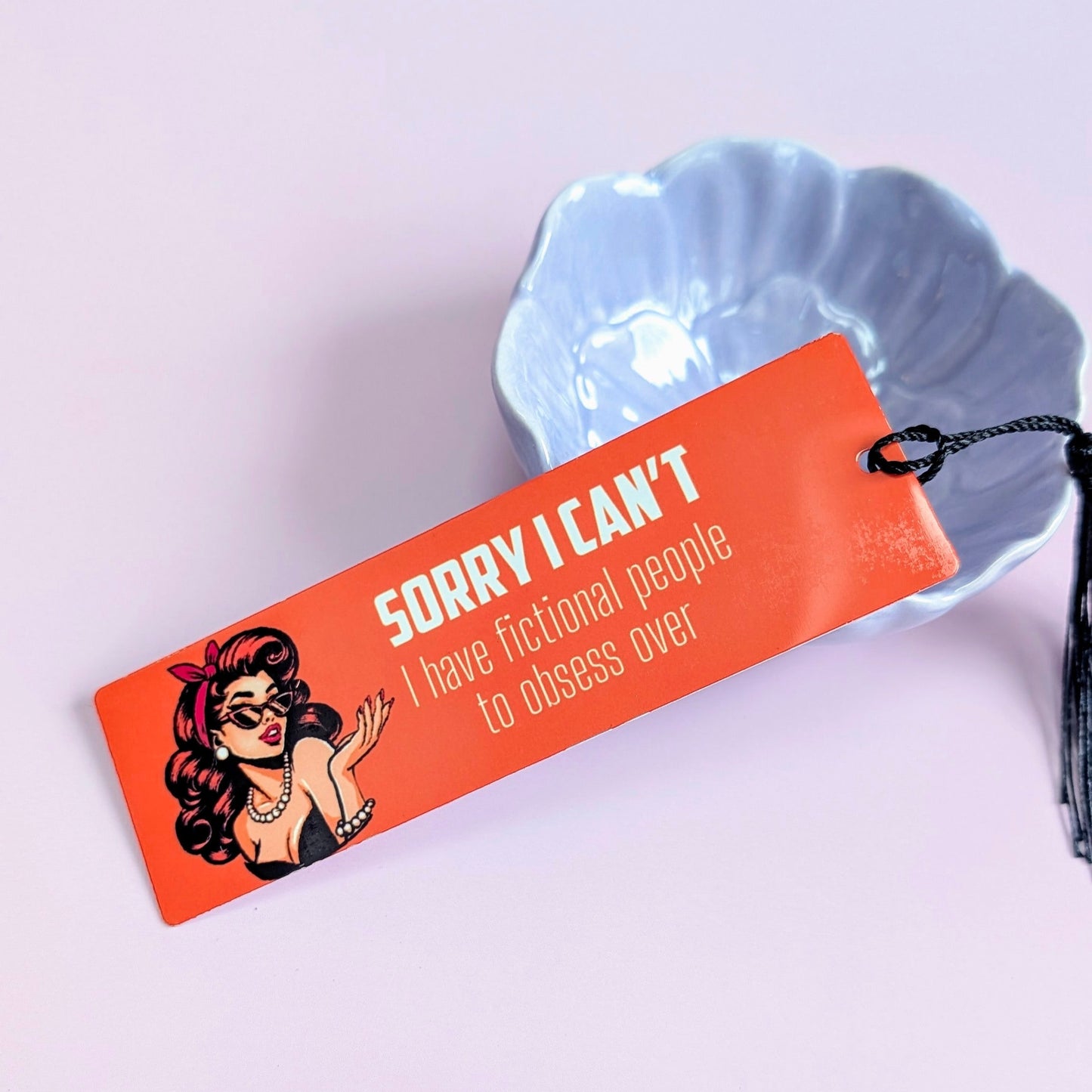 Bookmark with a character design and text on an orange background, placed on a light purple surface.
