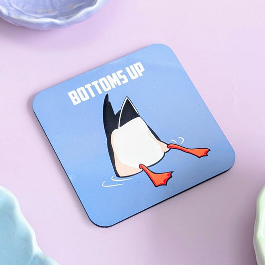 Coaster with a duck diving under water, and its tail feathers in the air with 'Bottoms Up' text on a blue background