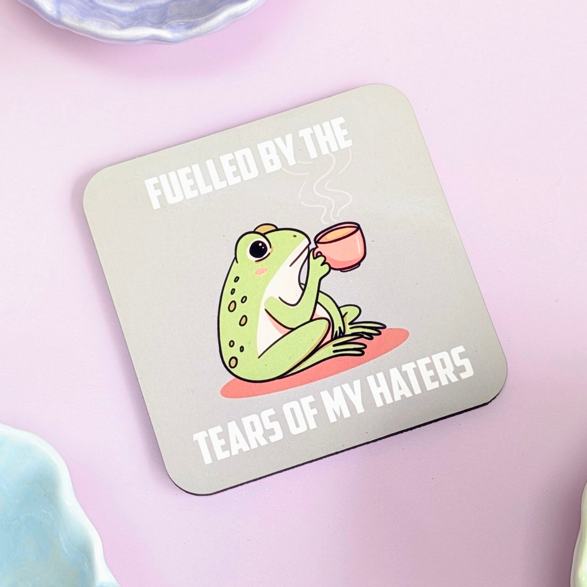 Coaster with a frog illustration and text "fuelled by the tears of my haters" on a green background
