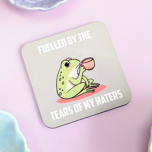 Coaster with a frog illustration and text "fuelled by the tears of my haters" on a green background