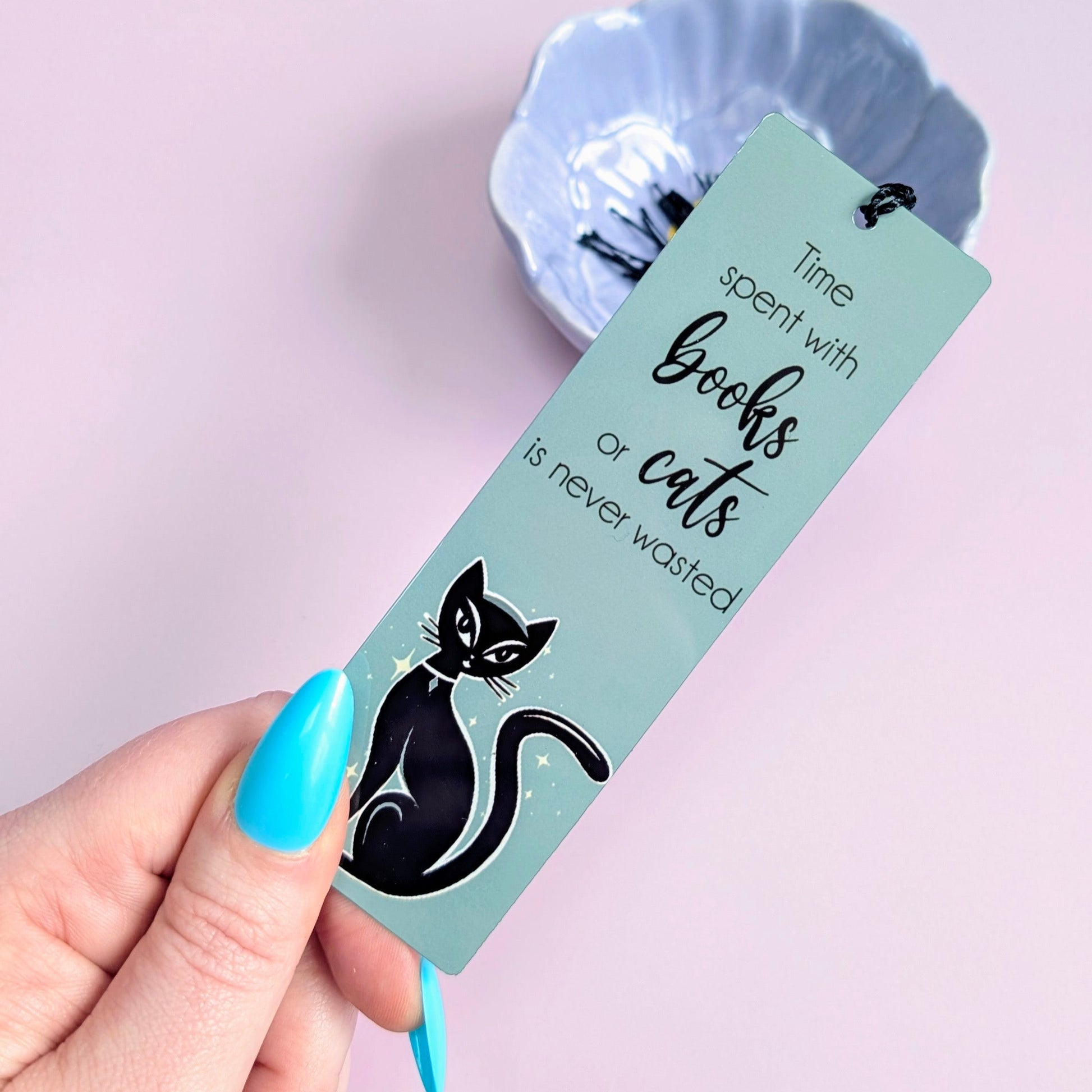 Bookmark with a black cat illustration and text held by a hand against a light purple background