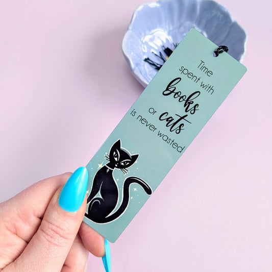 Bookmark with a black cat illustration and text held by a hand against a light purple background
